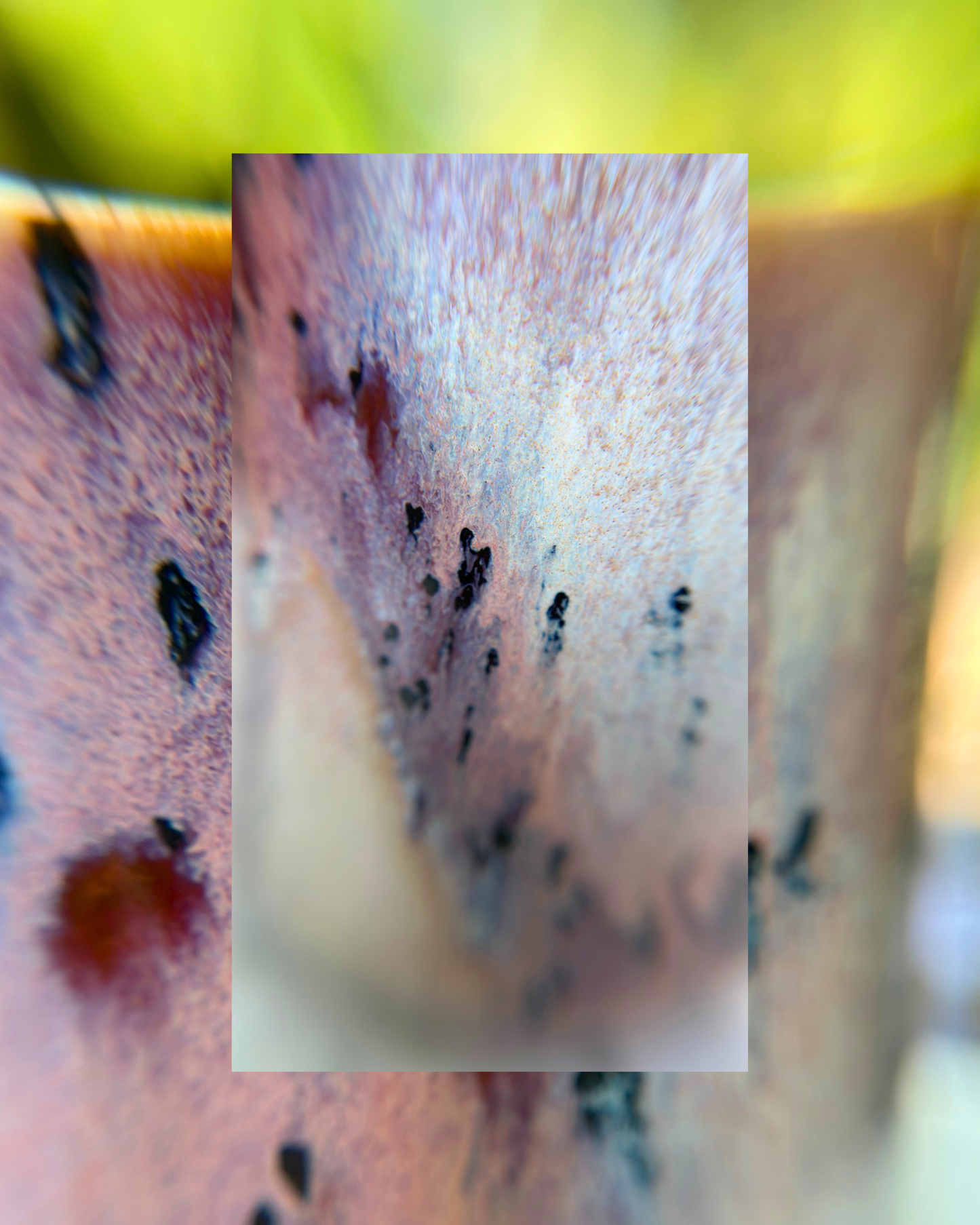 A close-up of a textured surface, likely a ceramic mug or pot, featuring a central rectangular inset showing a detailed view of dark spots and a reddish-brown mark on a pinkish-beige textured background.