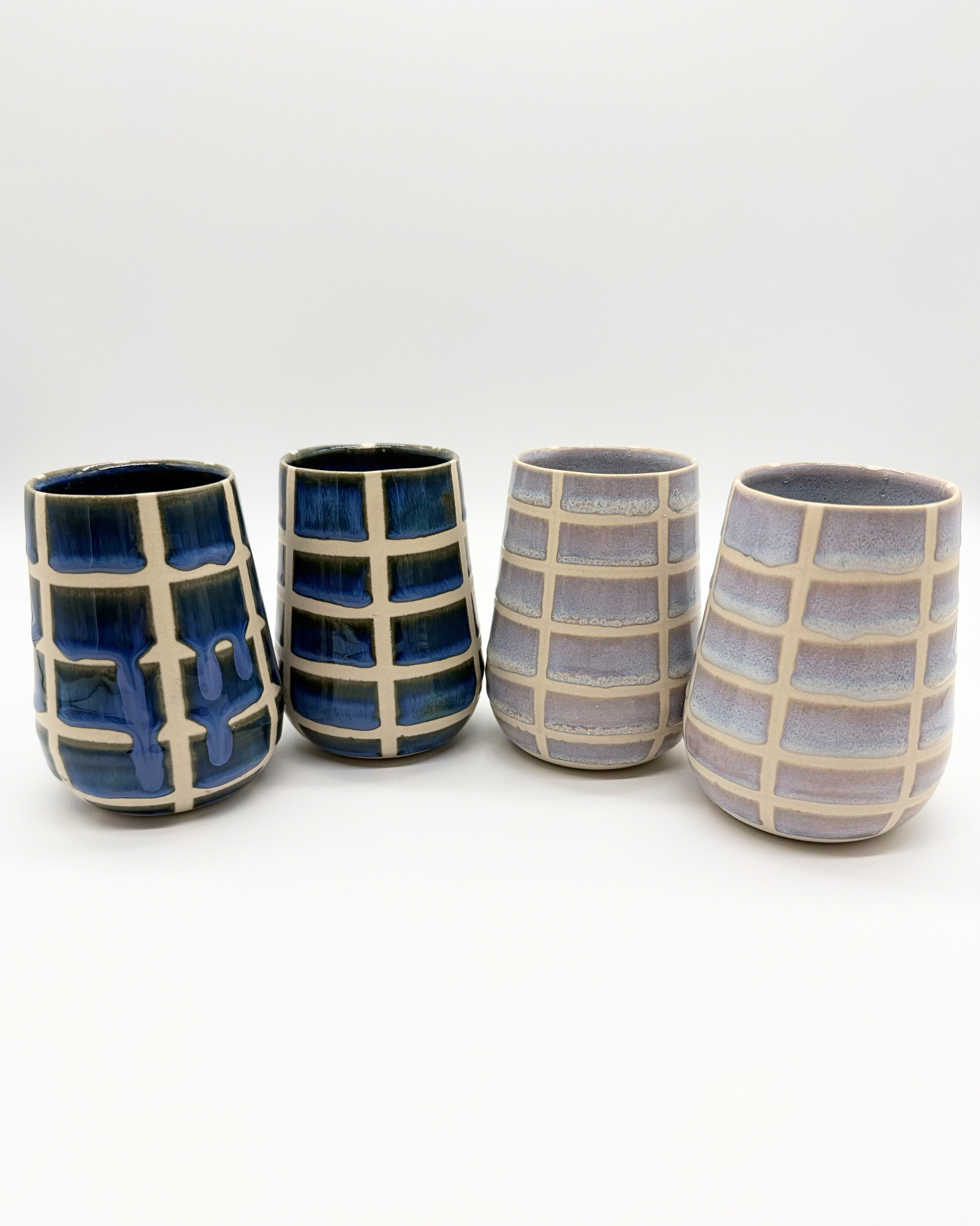 Four ceramic tumblers with checkered pattern on a white background