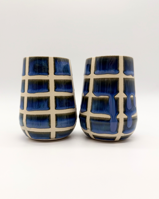 Two ceramic tumblers with blue and white grid pattern on a white background
