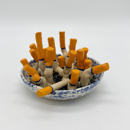 handmade blue-and-white spongeware ceramic ashtray sculpture filled with orange-tipped cigarette butts.