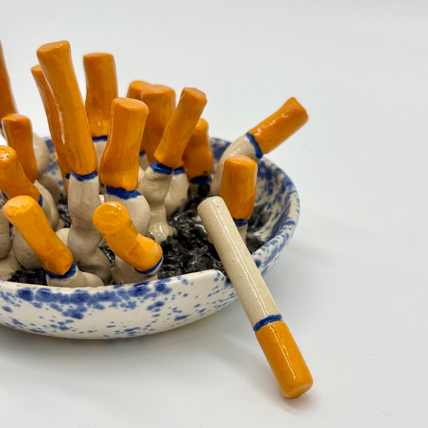 handmade blue-and-white spongeware ceramic ashtray sculpture filled with orange-tipped cigarette butts.