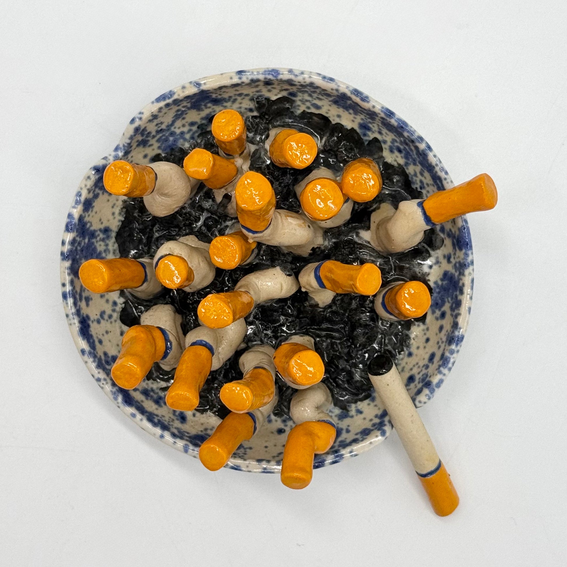 handmade blue-and-white spongeware ceramic ashtray sculpture filled with orange-tipped cigarette butts.