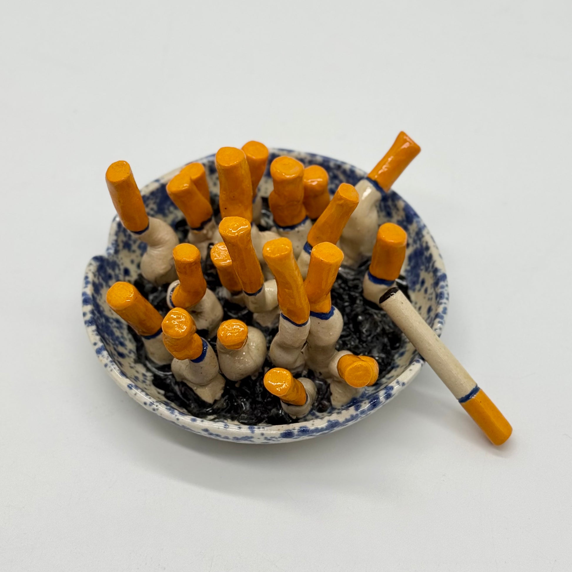 handmade blue-and-white spongeware ceramic ashtray sculpture filled with orange-tipped cigarette butts.