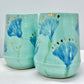 Two turquoise ceramic cups with blue floral designs on a white surface.