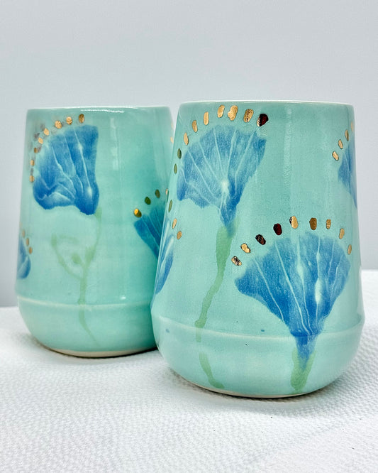 Two turquoise ceramic cups with blue floral designs on a white surface.