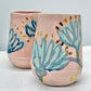 Two ceramic tumblers with floral designs on a light background