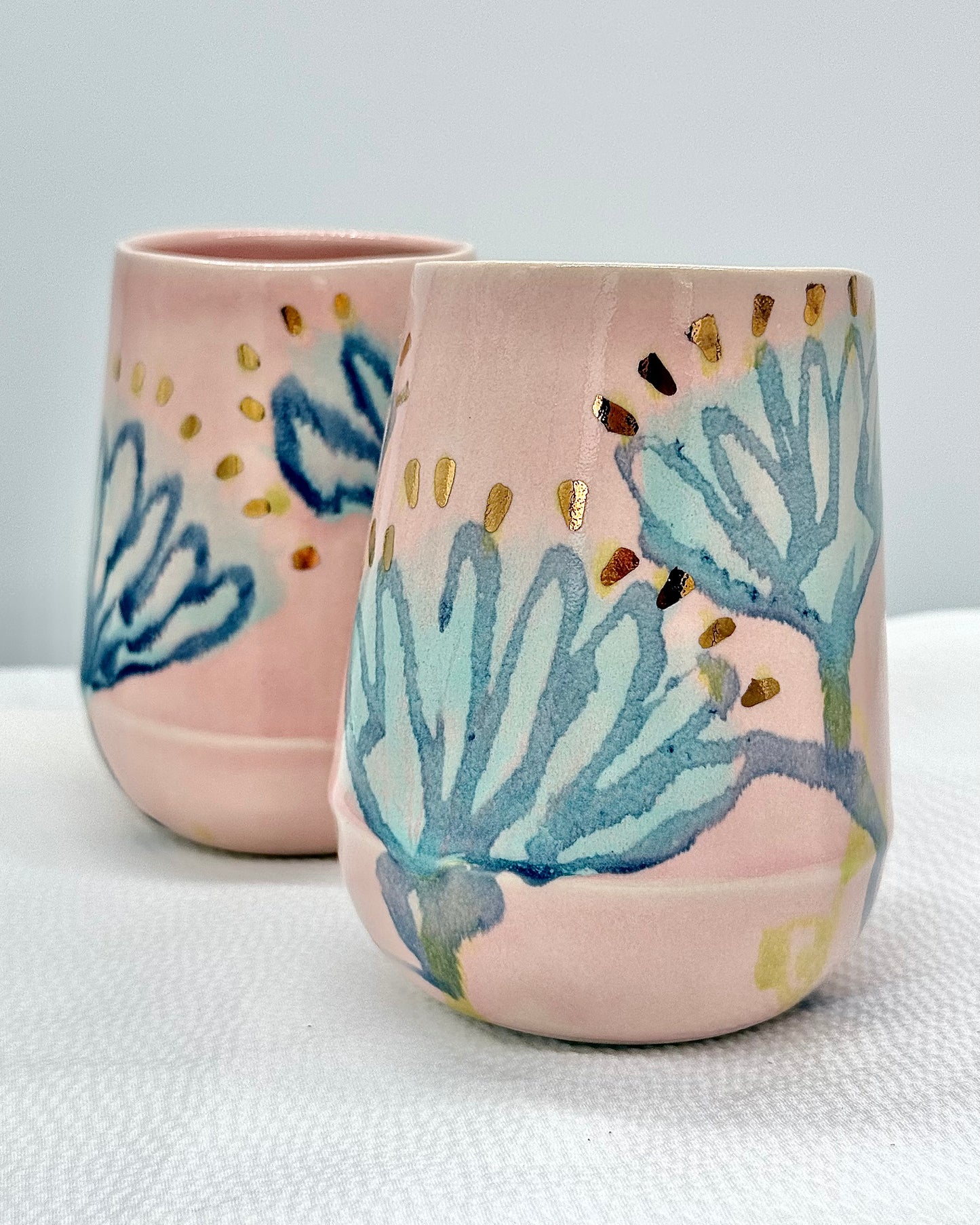 Two ceramic tumblers with floral designs on a light background