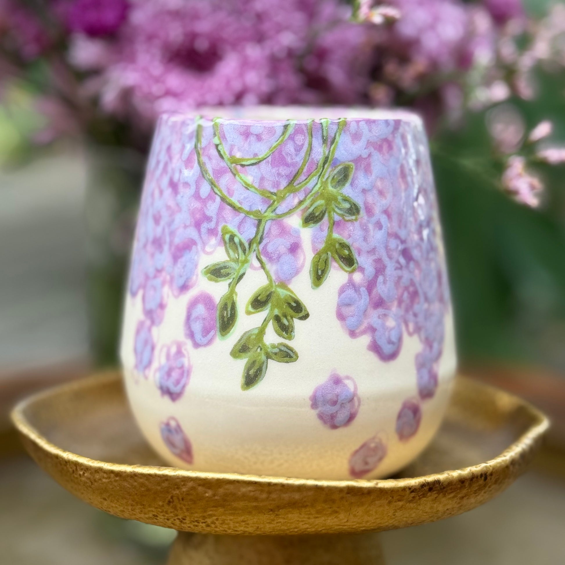 handmade and hand painted ceramic cups with handpainted wisteria, on a gold stand, surrounded by purple flowers of wisteria
