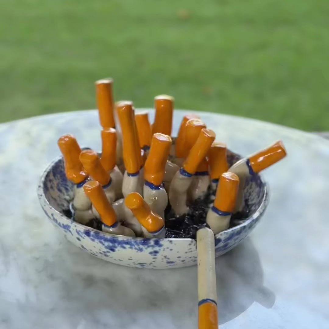 handmade blue-and-white spongeware ceramic ashtray sculpture filled with orange-tipped cigarette butts.